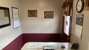 A reception desk with a glass partition, framed certificates on the wall, a clock, and a calendar. - The Village Motel (Eldora)