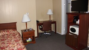 A hotel room with a bed, two bedside tables with lamps, a desk with a chair, a television, and a microwave. - The Village Motel (Eldora)