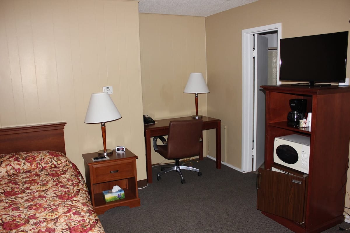 A hotel room with a bed, two bedside tables with lamps, a desk with a chair, a television, and a microwave.