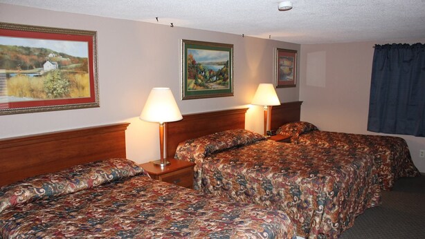 A hotel room with two beds, each with a patterned bedspread, two bedside lamps, and framed landscape paintings on the walls. - The Village Motel (Eldora)