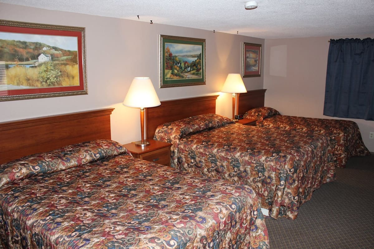 A hotel room with two beds, each with a patterned bedspread, two bedside lamps, and framed landscape paintings on the walls.