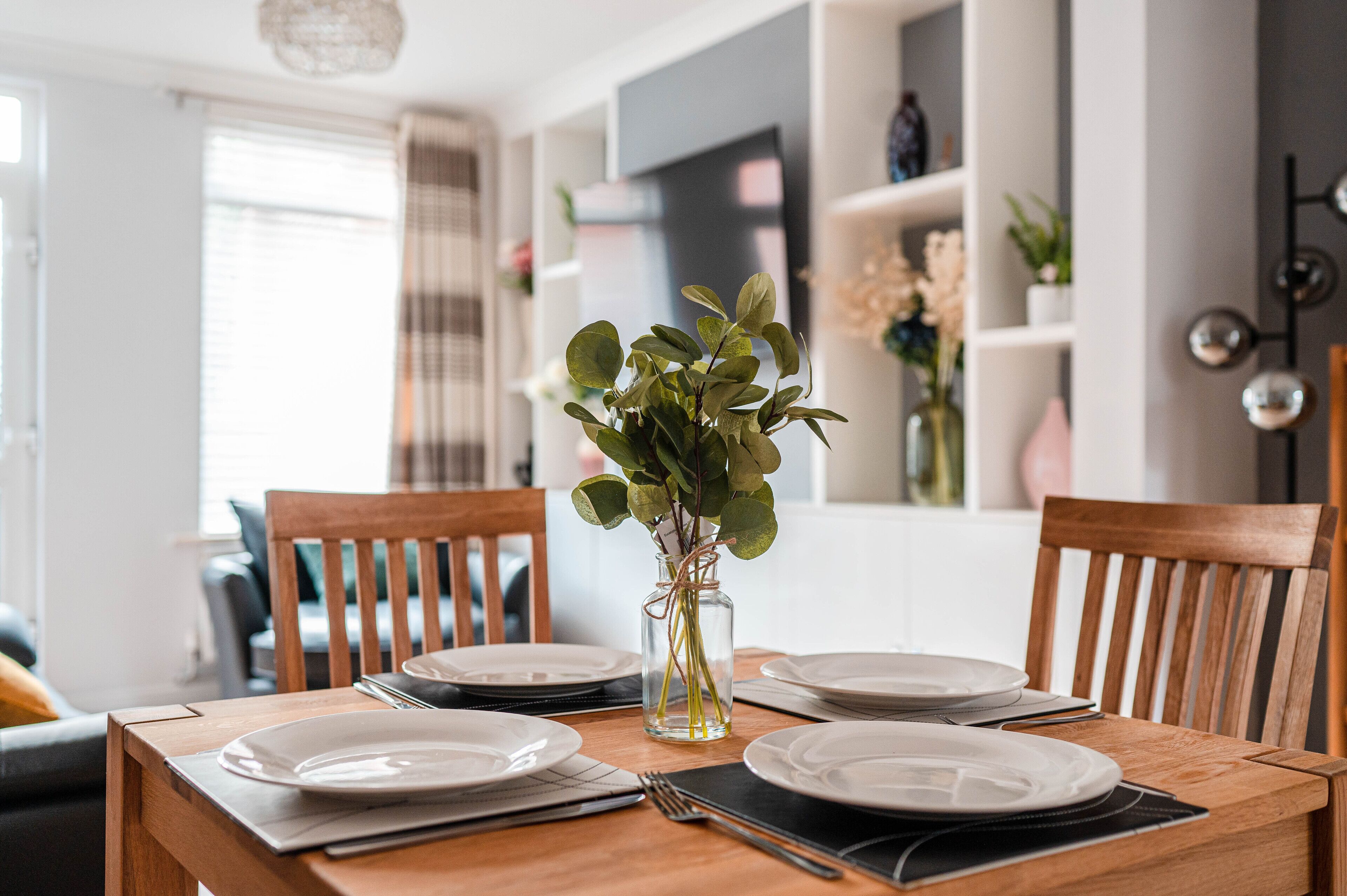 Une table à manger dressée avec des assiettes, un vase contenant des plantes vertes et un téléphone intelligent posé sur la table.