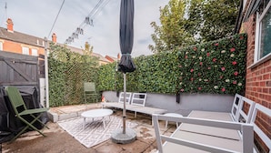 A patio area with a round table and white chairs, a covered umbrella, and a brick wall with climbing roses.