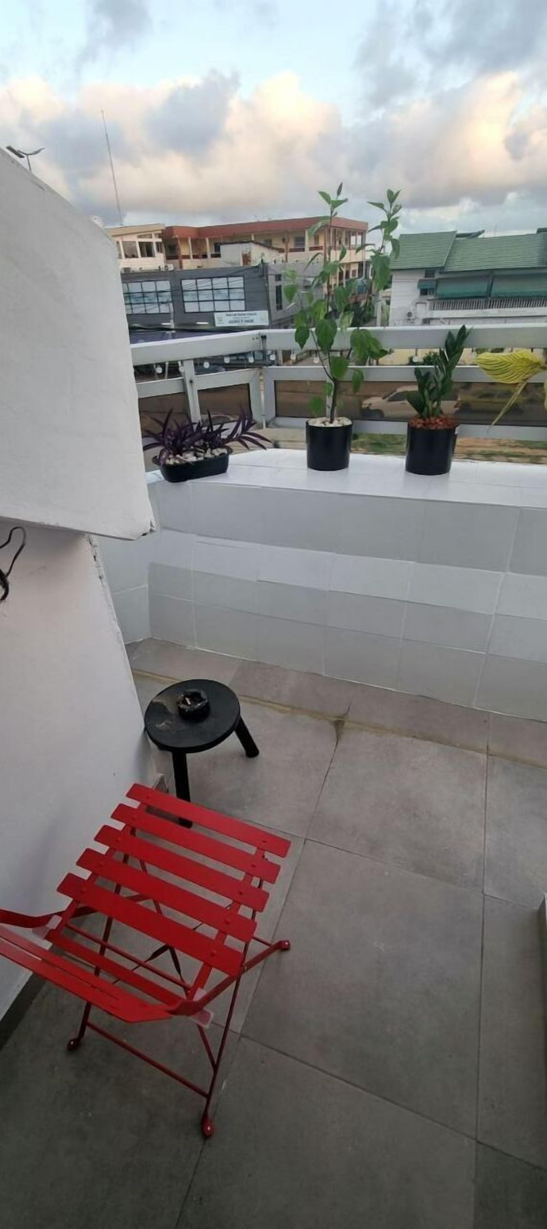 A small outdoor balcony with a red metal chair, a small round table, and potted plants.