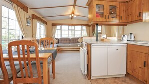A compact kitchen with wooden cabinets, a built-in dishwasher, and a dining area with a table and chairs. - Little Malory (Launceston)