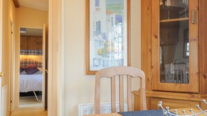 A cozy room with a wooden dining table, a chair, a bed with a plaid headboard, and a framed painting on the wall. - Little Malory (Launceston)