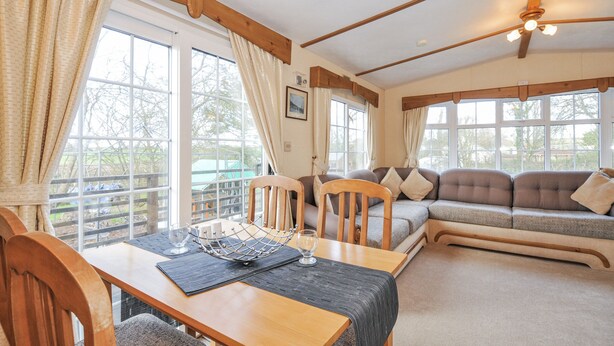 A cozy room with a wooden dining table, a sofa, and large windows offering a view of the outdoors. - Little Malory (Launceston)