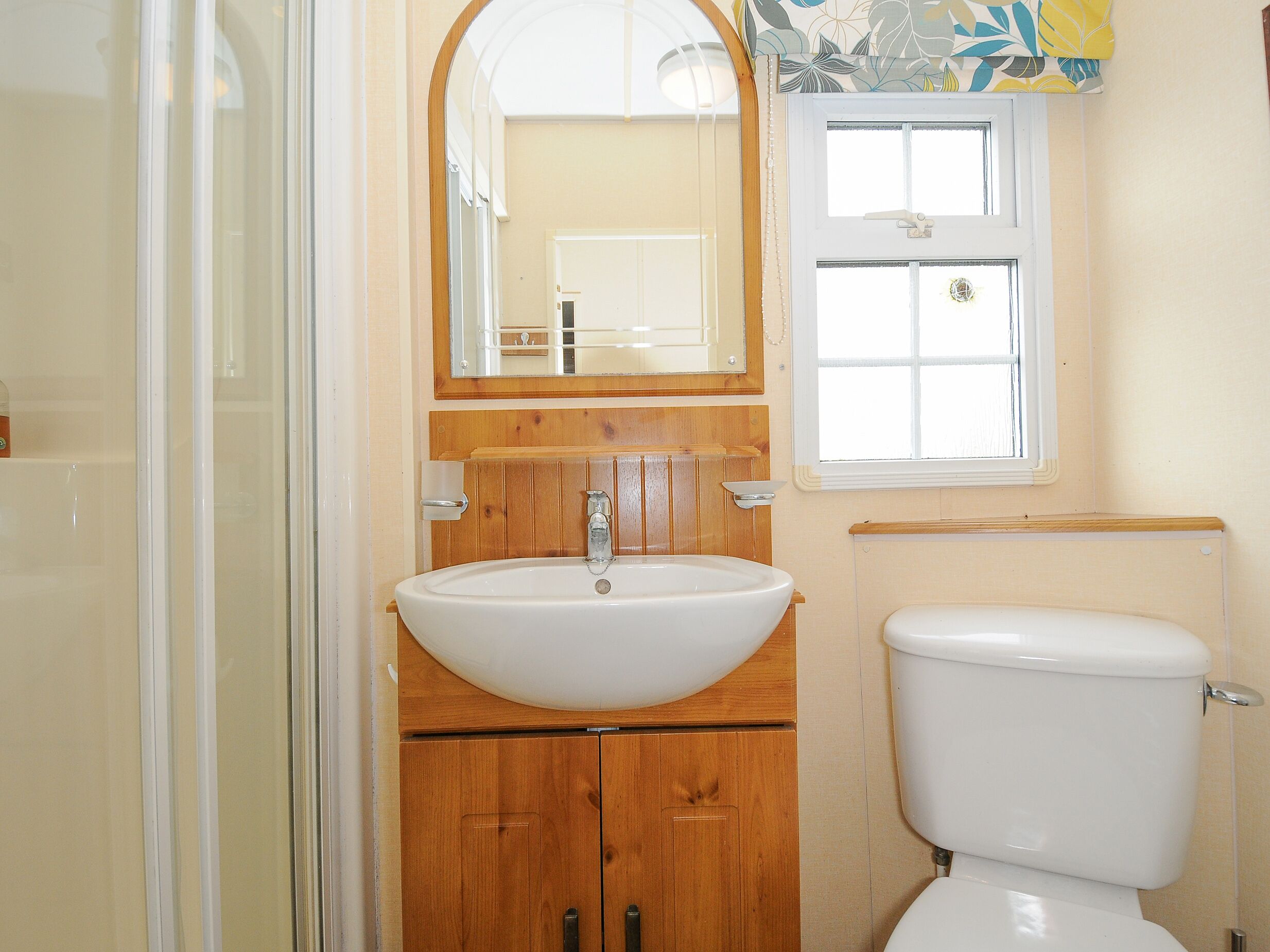A bathroom with a wooden vanity, a white sink, a mirror, and a toilet.