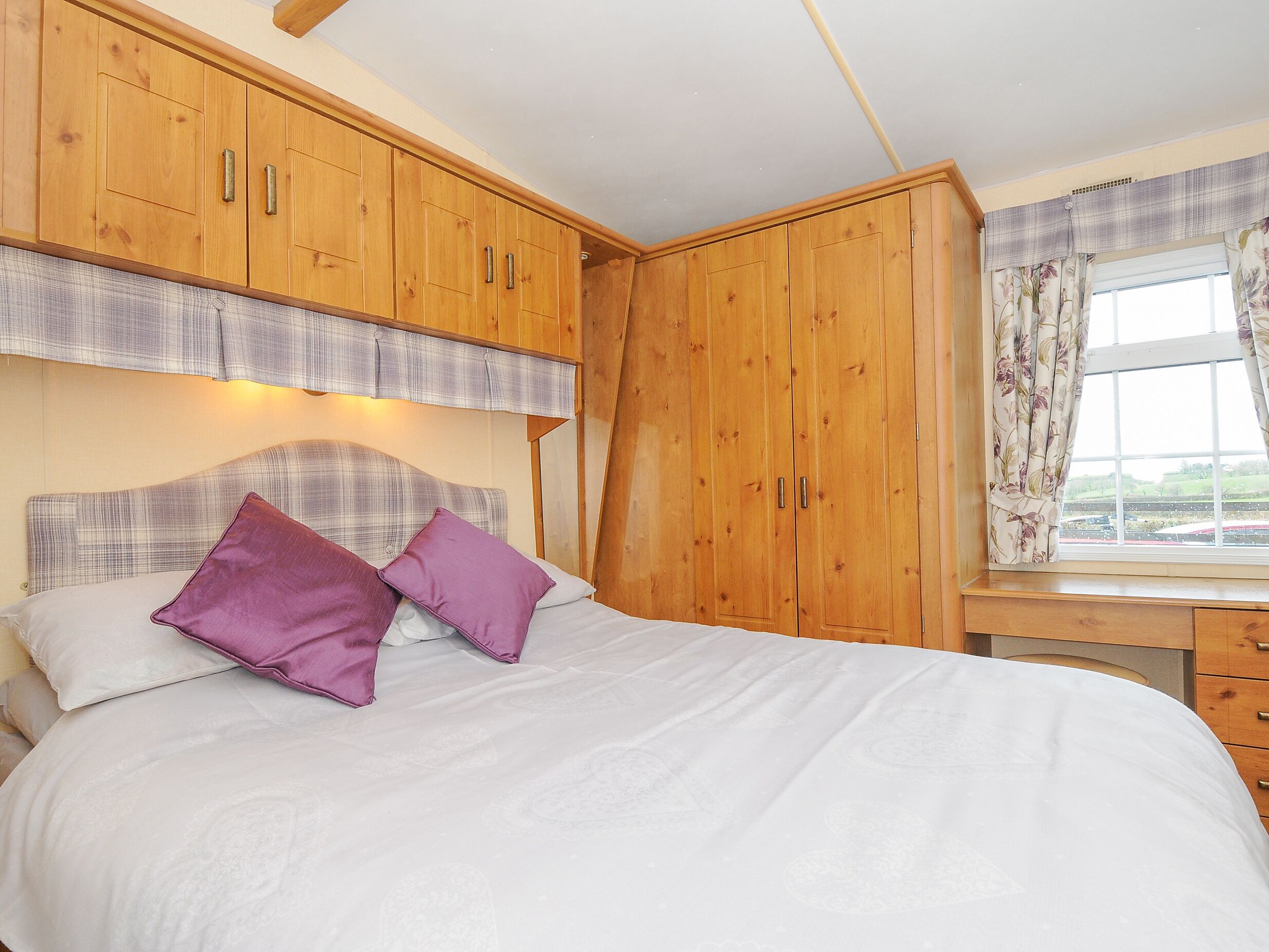A bedroom with a large bed, wooden wardrobe, and a window with curtains.