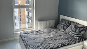 A modern bedroom with a bed, a window, and a hanging light fixture. - 1-bed Top Floor Apartment in Warszawa (Warsaw)