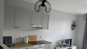 A modern kitchen with grey cabinets, a wooden countertop, a built-in oven, and a white dining area with a TV. - 1-bed Top Floor Apartment in Warszawa (Warsaw)