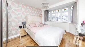 Een slaapkamer met een bed, nachtkastje, lamp en een raam met gordijnen.