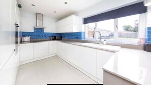 Een moderne keuken met witte kasten, een blauwe achterwand en een raam met uitzicht op het omliggende landschap.