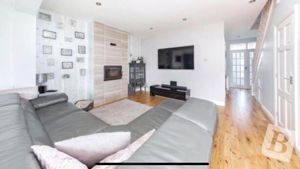 Een moderne woonkamer met een grijze hoekbank, een flatscreen televisie aan de muur en een open haard.