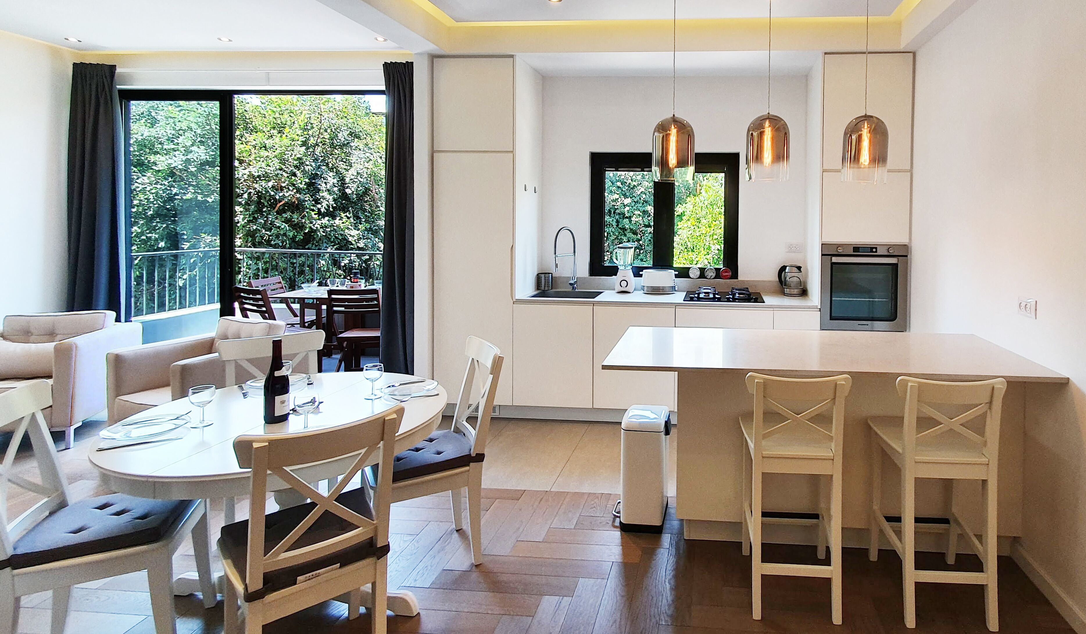 Une cuisine moderne dotée d’un îlot central, d’un coin repas avec une table ronde et des chaises, et offrant une vue sur la verdure environnante.