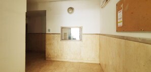 Um corredor com piso ladrilhado, uma porta à esquerda, um luminar na parede e um mural à direita.