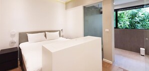 Quarto moderno com uma cama grande, uma mesa de cabeceira e vista para o verde através de uma janela.