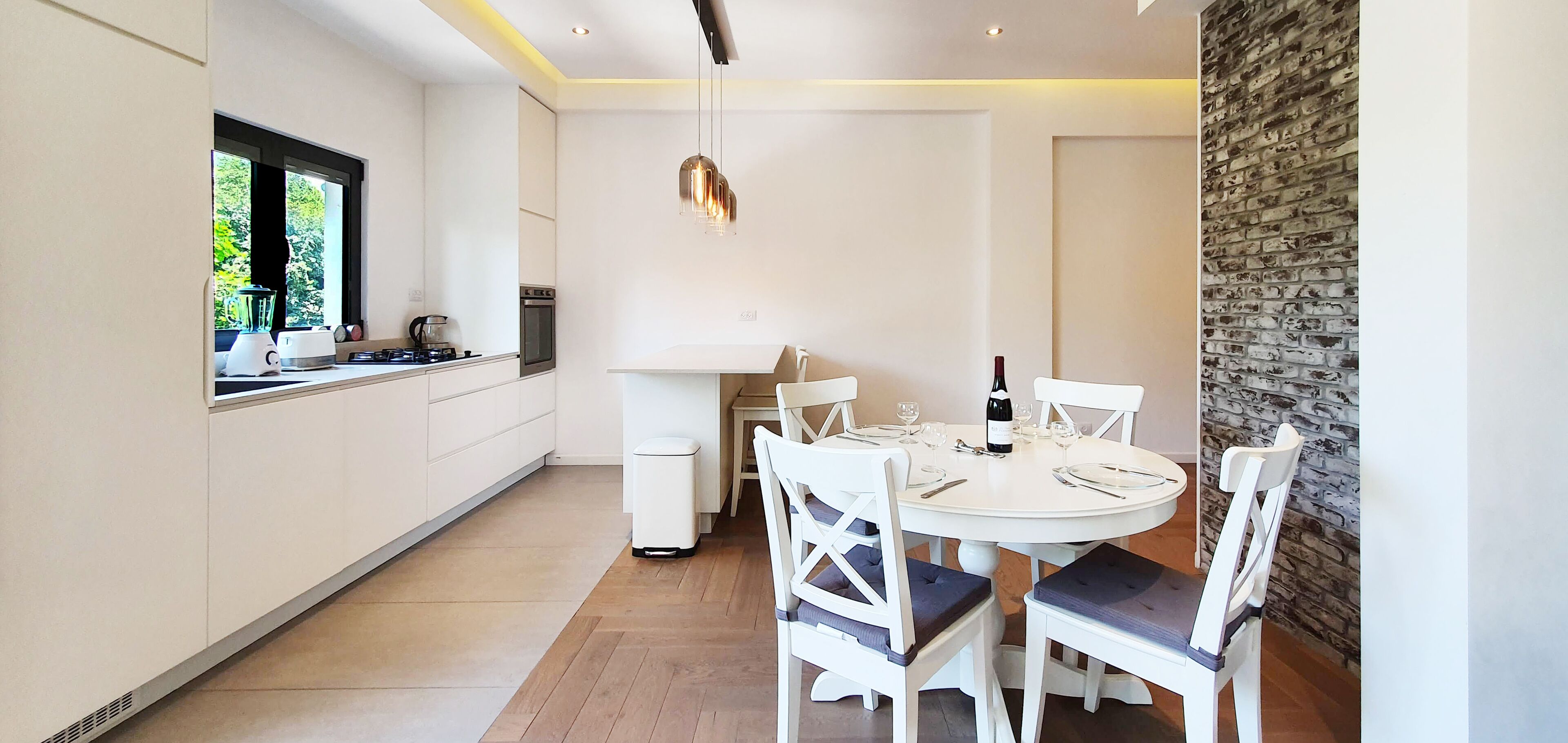 Una cocina moderna con armarios blancos, una mesa de comedor para cuatro personas y una pared de acento de piedra.