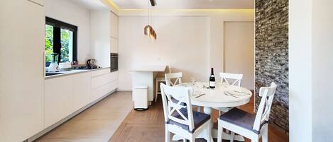 Una cocina moderna con armarios blancos, una mesa de comedor para cuatro personas y una pared de acento de piedra.