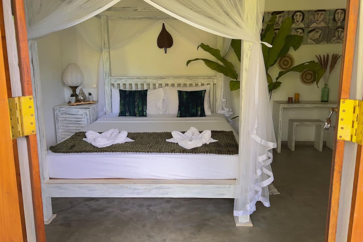 A bed with a canopy, a bedside table with a lamp, and a wall with artwork.