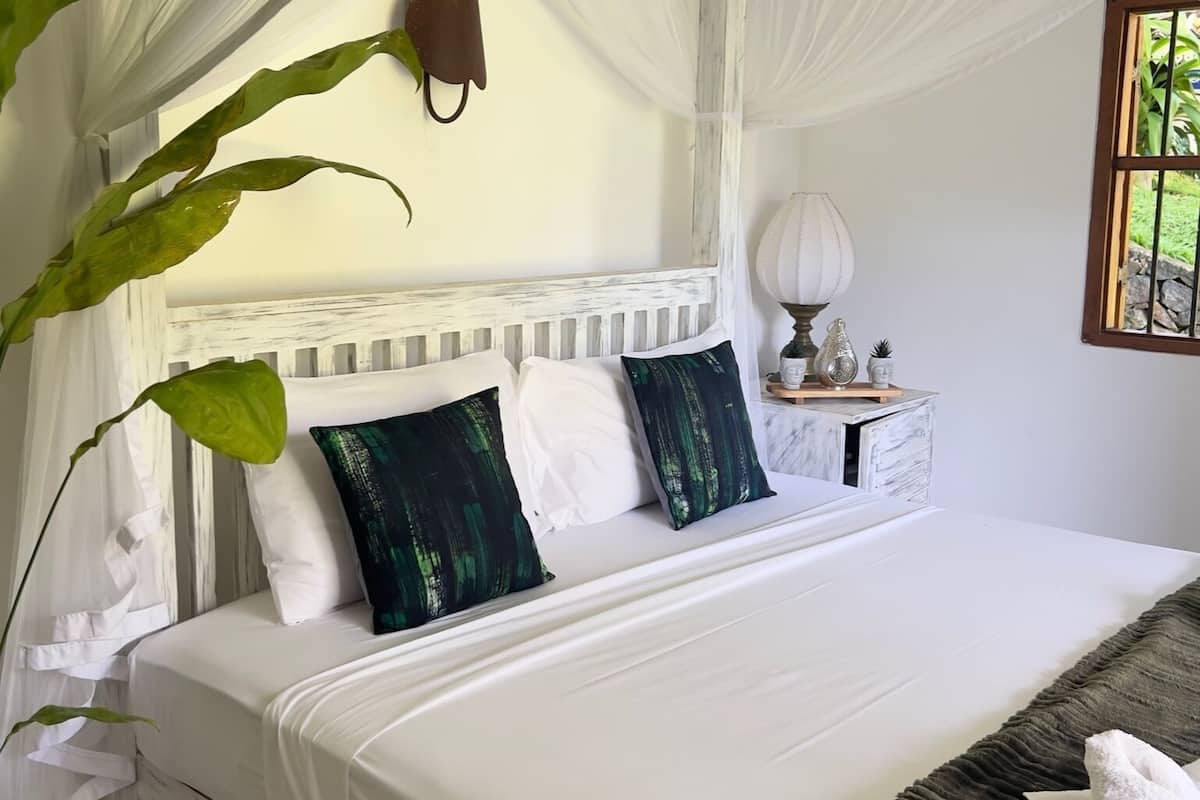 A bed with white bedding, a canopy, and a bedside table with a lamp and decorative items.