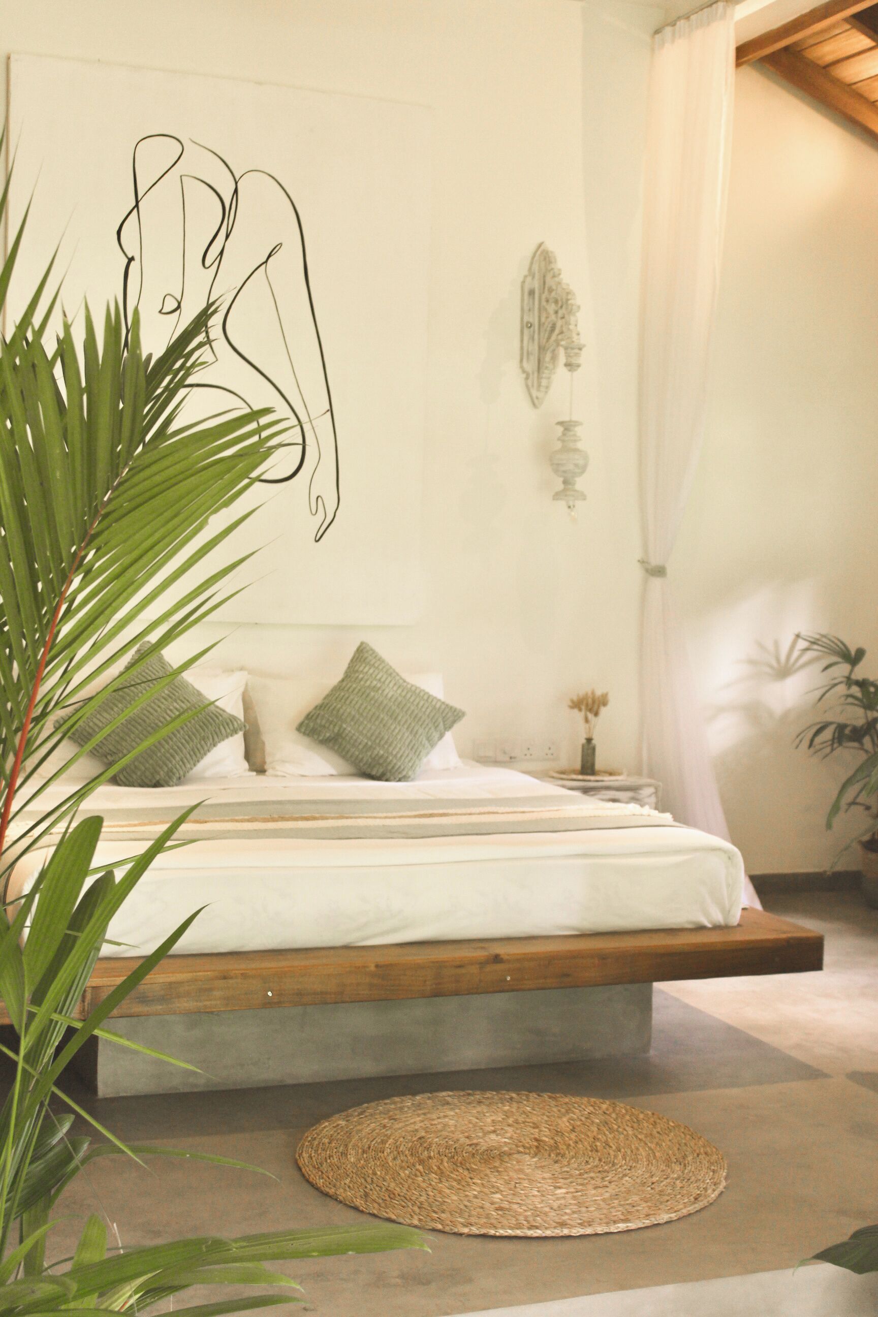 Un dormitorio con una cama baja sobre plataforma, una mesita de noche con un florero y una lámpara fijada a la pared.