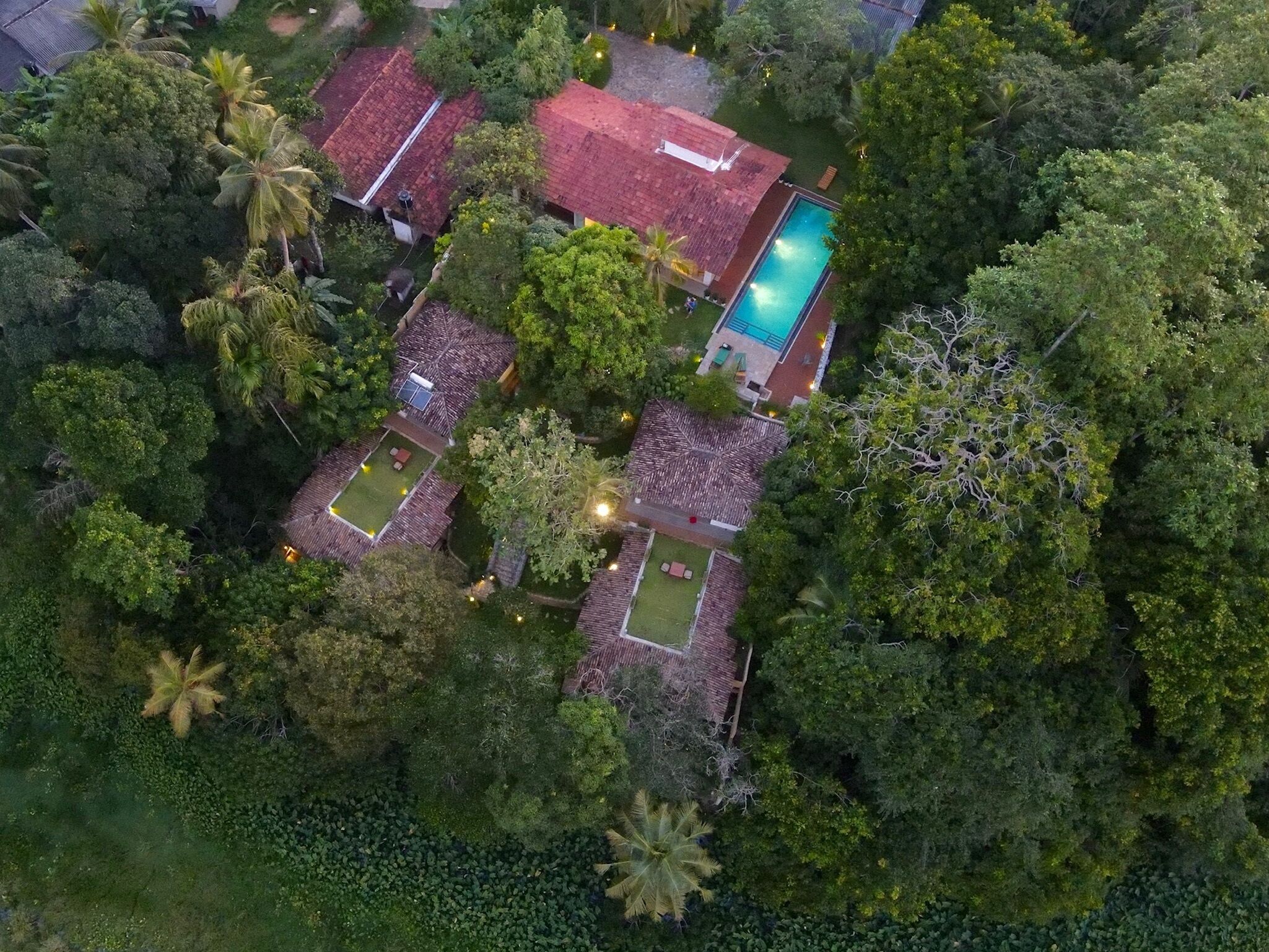 Una vista aerea di una zona residenziale con diverse case, una piscina e rigogliosa vegetazione.