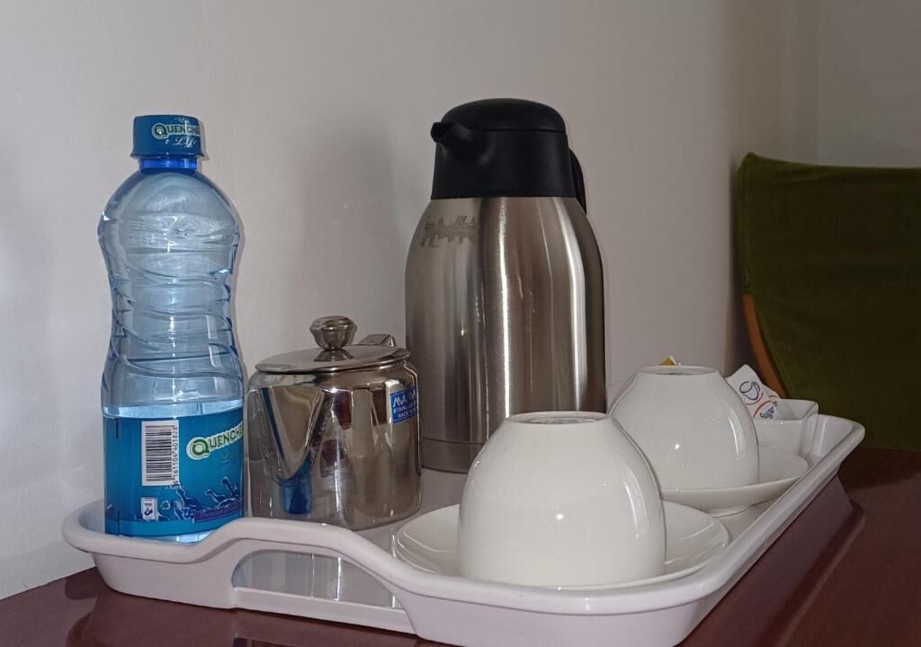 A tray with a water bottle, a thermos, a container, and two white cups.