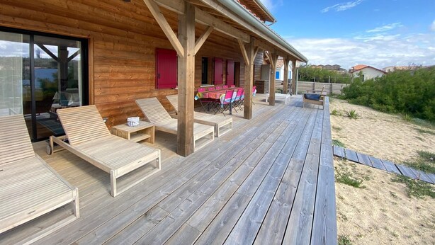 Een houten terras met lounge stoelen en een overdekt gedeelte met tafels en stoelen.