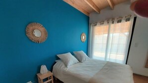 Een slaapkamer met een bed, nachtkastje, spiegel en een raam met gordijnen.