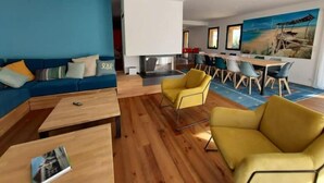 Een moderne woonkamer met een blauwe bank, gele fauteuils en een eethoek met een groot schilderij.
