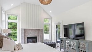 Ein Schlafzimmer mit einem großen Bett, einem Fernseher, einem Kamin und Blick ins Grüne.