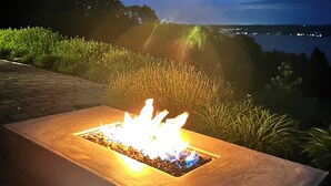 Ein rechteckiges Outdoor-Feuerbecken mit freiem Blick auf die umliegende Landschaft und einem Gewässer im Hintergrund.