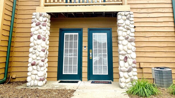 A two-story building with a balcony, two doors, and a small garden area.