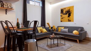 Uma sala de estar moderna com um sofá cinzento, cadeiras pretas, uma mesa de jantar com uma garrafa e um copo, e um quadro na parede.