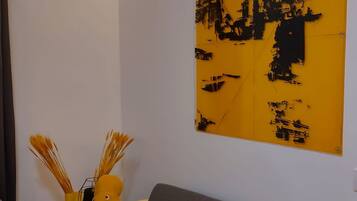 Una sala de estar moderna con un sofá gris, cojines amarillos y plateados, y un cuadro abstracto grande en la pared.