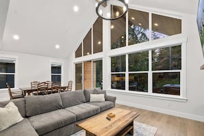 A spacious living room with a large gray sectional sofa, a wooden coffee table, and a dining area with a wooden table and chairs.
