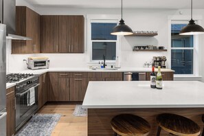 A modern kitchen with wooden cabinets, a built-in oven, a microwave, a large island, and pendant lighting.