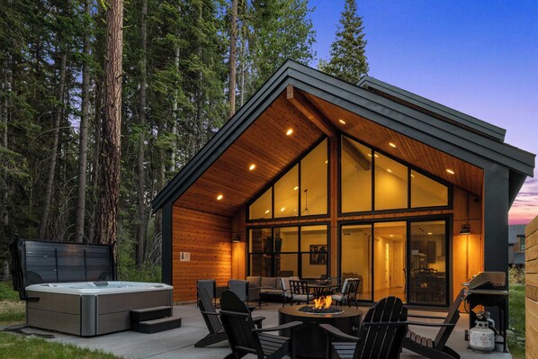 A modern cabin with a hot tub, outdoor seating, and a large glass window.
