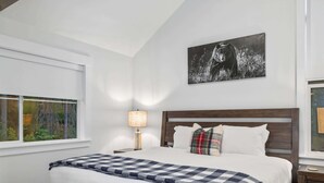 Une chambre à coucher avec un grand lit, une table de chevet, une lampe, une fenêtre donnant sur un beau paysage et un tableau accroché au mur.