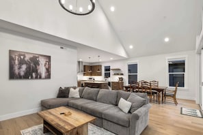 A modern living room with a gray sectional sofa, wooden coffee table, and a painting of horses.
