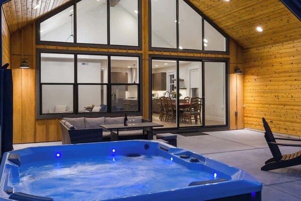 Ein Whirlpool in einem Zimmer mit großen Fenstern, Holzwänden und einem Essbereich, der durch die Fenster sichtbar ist.