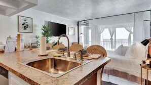 A modern kitchen with a large granite countertop, stainless steel sink, and a dining area with wicker chairs. - 1920s Speakeasy with Waterview & Heated Pool (Tampa)