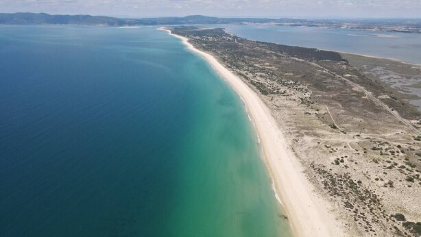 Luftaufnahme einer Küstenregion mit einem langen, sandigen Strand und einem tiefblauen Meer.