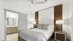 Un dormitorio con cama, mesitas de noche, ventilador de techo y un espejo grande.