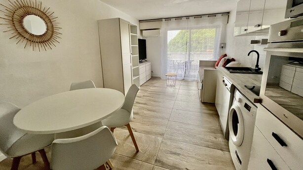 A compact kitchen with a dining area, a washing machine, and a TV. - Studio, Avec Terrasse, Tout Confort Climatisé et Parking Privatif en Sous-sol (Hyères)