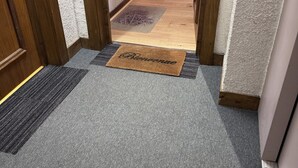 A hallway with a grey carpet, a doormat with 'Bienvenue' written on it, and a wooden door on the left. - Charming Bright Spacious Village Walk to lift Hike (Praz Sur Arly)