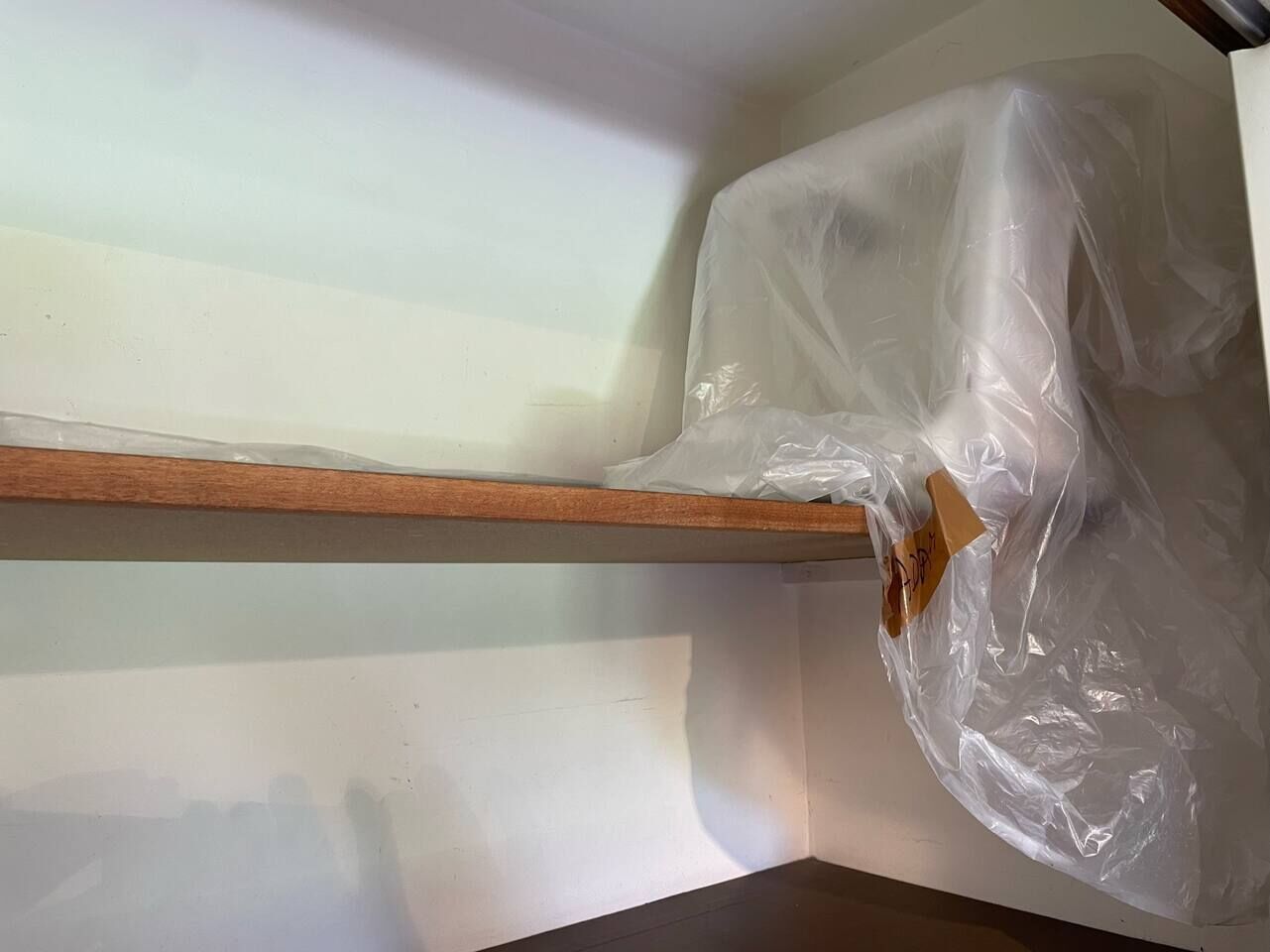 Un coin de pièce avec une étagère en bois et un sac en plastique qui y est suspendu.