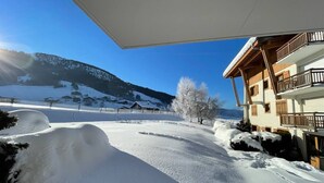 A snow-covered landscape with a wooden building featuring balconies and a view of a mountain range. - Charming Bright Spacious Village Walk to lift Hike (Praz Sur Arly)