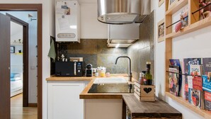 A compact kitchen with a built-in stove, a sink, and a microwave. There is a wooden shelf with books and a small cabinet with a heart-shaped cutout. - Cozy, bright, comfortable penthouse, 2 min from metro Dergano.  (Milano)
